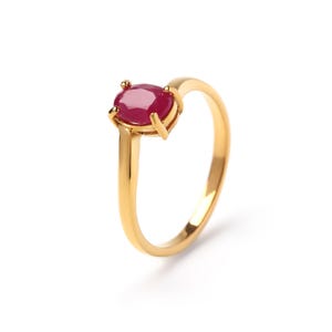 May include: A gold ring featuring a vibrant, oval-cut ruby gemstone. The ruby is set in a four-prong setting, and the band is a simple, polished gold. The ring is displayed against a white background, highlighting the gemstone's rich color.