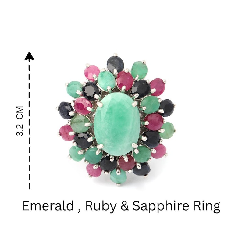 Puede incluir: Un anillo de plata con una gran esmeralda ovalada de color verde claro, rodeada de piedras preciosas m&aacute;s peque&ntilde;as en tonos rosa, verde y azul oscuro. El anillo mide aproximadamente 3,2 cm de largo. El texto de la imagen dice "Emerald, Ruby & Sapphire Ring."