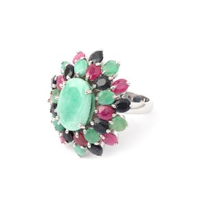 Puede incluir: Un anillo de plata con una gran piedra ovalada de color verde claro en el centro, rodeada de piedras m&aacute;s peque&ntilde;as en forma de l&aacute;grima en tonos verdes, rojos y negros. El anillo tiene una banda pulida y reflectante.