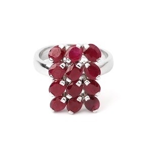 May include: A silver ring featuring a cluster of oval-cut, deep red gemstones. The gemstones are arranged in a cascading pattern, creating a unique and eye-catching design. The ring's band is smooth and polished, complementing the vibrant stones.