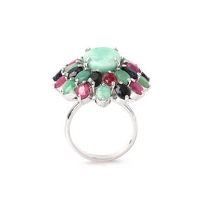 Puede incluir: Un anillo de plata con una piedra preciosa grande, ovalada y verde claro, rodeada por un grupo de piedras preciosas m&aacute;s peque&ntilde;as y coloridas. Las piedras m&aacute;s peque&ntilde;as son de varios tonos de verde, rojo, rosa y negro. El anillo tiene un acabado pulido y reflectante.