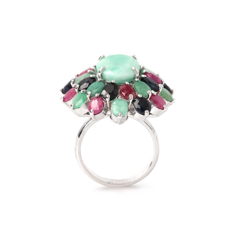 Puede incluir: Un anillo de plata con una piedra preciosa grande, ovalada y verde claro, rodeada por un grupo de piedras preciosas m&aacute;s peque&ntilde;as y coloridas. Las piedras m&aacute;s peque&ntilde;as son de varios tonos de verde, rojo, rosa y negro. El anillo tiene un acabado pulido y reflectante.