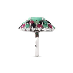 Puede incluir: Un anillo de plata con una gran gema rectangular verde claro en el centro, rodeada de gemas m&aacute;s peque&ntilde;as de colores verde, rojo y negro. La banda del anillo es de plata pulida.