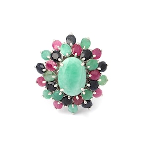 May include: A silver ring featuring a large, oval-shaped, light green gemstone at the center, surrounded by a cluster of smaller, colorful gemstones in shades of pink, green, and dark blue. The ring has a floral design.