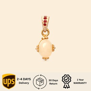 Può includere: Un ciondolo in oro con una pietra bianca centrale di forma ovale, accentuato da piccoli intarsi circolari rossi sulla contromaglia. Il design presenta decorazioni in metallo dorato sulla parte superiore e inferiore della pietra preziosa.