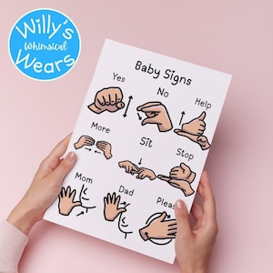 Pair of hands holding a paper print titled Baby Signs showing hand gestures for words like yes, no, and help.