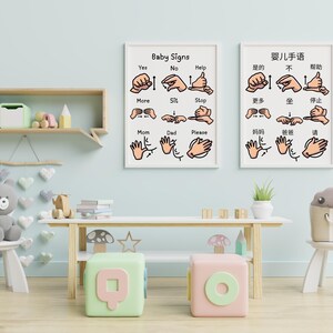 Two framed baby sign language posters in English and Chinese hanging on a light blue wall in a playroom.