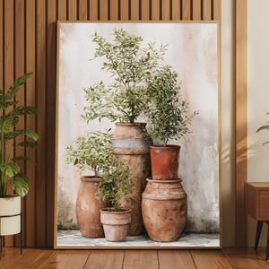 May include: A framed wall art print depicting a collection of five terracotta pots of varying sizes, each containing a small green plant. The pots are arranged in a cluster against a neutral, textured background, all enclosed in a thin wooden frame.
