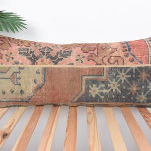 May include: A long rectangular pillow with a colorful patchwork design. The pillow is made from a vintage rug with a variety of colors and patterns, including red, pink, blue, and green. The pillow is perfect for adding a touch of bohemian style to any room.