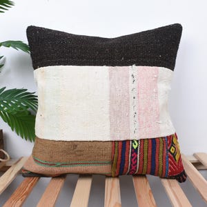 May include: A patchwork pillow cover with a black, white, brown, pink, and multi-colored geometric pattern. The pillow cover is made of woven fabric and has a rustic, bohemian style.