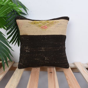 May include: A brown and beige patterned cushion with a geometric design. The cushion is sitting on a wooden slatted surface.