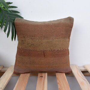 Könnte beinhalten: Ein braunes und beigefarbenes gewebtes Kissen mit einem subtilen Ombre-Effekt. Das Kissen ist aus einem weichen, strukturierten Stoff gefertigt und hat eine quadratische Form.