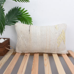 May include: A white rectangular cushion with a subtle yellow geometric pattern. The cushion is sitting on a wooden slatted surface.