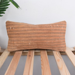 May include: A brown and beige striped lumbar pillow with a woven texture. The pillow is lying on a wooden slatted surface.