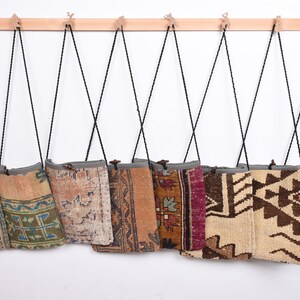 May include: Eight colorful woven tapestry bags hanging on a wooden rack. The bags are made of different fabrics and patterns, including geometric designs, floral motifs, and abstract patterns. The bags are all different sizes and shapes, but they are all hung on the same rack.