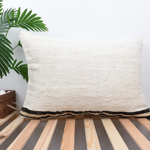 May include: A white rectangular pillow with a black and brown striped border. The pillow is sitting on a wooden slatted surface.