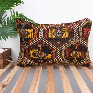 May include: A rectangular pillow with a brown background and a colorful geometric pattern in shades of yellow, red, and orange. The pillow is made of woven fabric and has a fringed edge.
