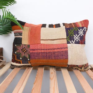 Può includere: Un cuscino rettangolare in patchwork con una varietà di colori e motivi, tra cui rosso, arancione, marrone, beige e viola. Il cuscino è realizzato in tessuto tessuto e ha un bordo sfilacciato.