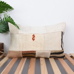 May include: A white patchwork pillow with black and brown stripes on the edges. The pillow has a small orange embroidered design in the center.