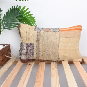 May include: A rectangular patchwork pillow with a beige, brown, orange, and blue color scheme. The pillow is made of woven fabric and has a rustic, bohemian style.