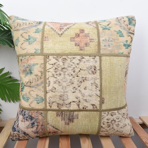 May include: Square patchwork cushion with a vintage rug design. The cushion features a beige, green, and blue colour palette with floral and geometric patterns. The cushion is made of multiple fabric squares sewn together.