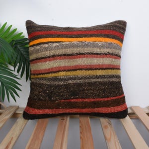 Puede incluir: Una almohada de tiro a rayas con un esquema de color marrón, naranja y beige. La almohada está hecha de tejido tejido y tiene un aspecto rústico y artesanal.