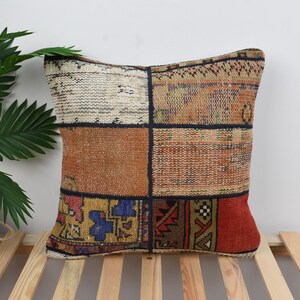 May include: A patchwork pillow cover with a variety of colors and patterns, including red, orange, brown, and blue. The pillow cover is made from a woven fabric and has a fringed edge.