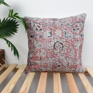 May include: A red, white, and blue patterned throw pillow with a floral design. The pillow is sitting on a wooden slatted surface.