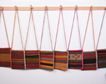 May include: Eight colorful woven tapestry bags hanging on hooks. The bags are made of different colors and patterns, including red, orange, yellow, green, blue, and purple.