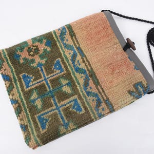 May include: A small, rectangular bag made from a woven rug with a geometric pattern in shades of blue, green, and beige. The bag has a black strap and a wooden toggle closure.