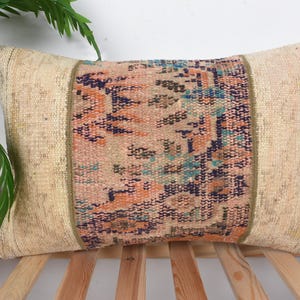May include: Rectangular decorative pillow with a central patterned panel in shades of peach, blue, and navy. The sides are a neutral beige, and the pillow is placed on a wooden surface. The pillow's design suggests a vintage or bohemian style.