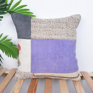 May include: A patchwork throw pillow with a purple, gray, and white design. The pillow is made of a soft, textured fabric and has a square shape.