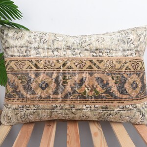 May include: Rectangular decorative pillow with a vintage rug design. The pillow features a beige and brown color scheme with intricate floral and geometric patterns. The pillow is placed on a wooden bed frame.
