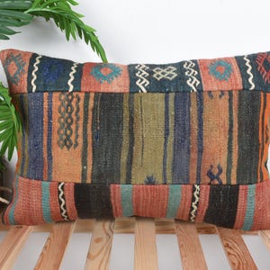 Könnte beinhalten: Rechteckiges Zierkissen mit Patchwork-Design. Das Kissen weist eine Mischung aus Farben wie Orange, Blau, Schwarz und Grün auf. Das Design umfasst geometrische Muster und vertikale Streifen, die dem Kissen Textur verleihen.