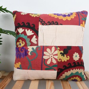 Peut inclure: Coussin décoratif rectangulaire avec un motif patchwork. Le fond est rouge avec des motifs floraux et géométriques blancs, jaunes, violets et verts. Le coussin est en tissu et présente un panneau central crème.