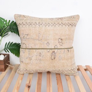May include: A beige throw pillow with a subtle pattern and a brown trim. The pillow is sitting on a wooden surface.