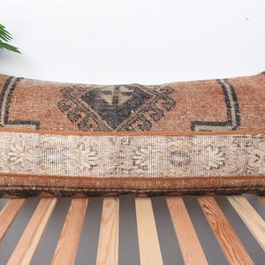 May include: Rectangular decorative pillow with a vintage rug design. The pillow features a central geometric pattern in black and brown, bordered by a cream and brown floral design. The pillow is approximately 30 inches long.