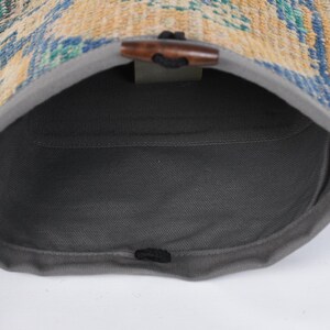 May include: A gray drawstring bag with a woven fabric top. The bag is open and the inside is visible. The woven fabric is a mix of blue, yellow, and green colors.