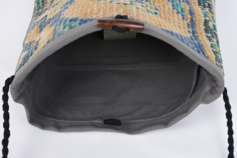 May include: A gray drawstring bag with a woven fabric top. The bag is open and the inside is visible. The woven fabric is a mix of blue, yellow, and green colors.
