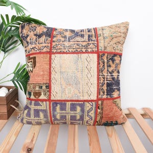 May include: A colorful patchwork throw pillow with a geometric pattern in shades of red, orange, blue, and beige. The pillow is made of woven fabric and has a fringed edge.