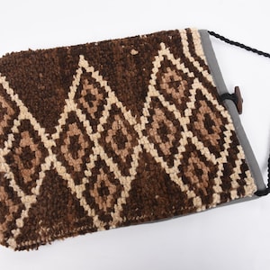 May include: A brown and cream woven bag with a geometric pattern. The bag has a black strap and a wooden button closure.