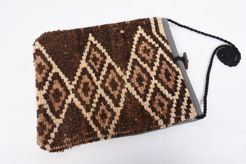 May include: A brown and cream woven bag with a geometric pattern. The bag has a black strap and a wooden button closure.