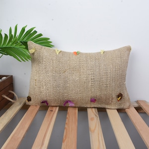 May include: A beige throw pillow with colorful embroidered details, resting on a wooden slatted surface.