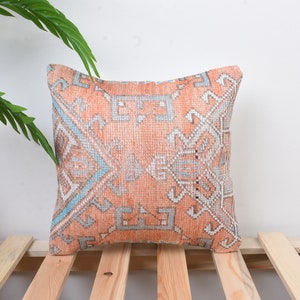 May include: A decorative throw pillow with a geometric pattern in shades of peach, blue, and white. The pillow is made of a soft, woven fabric and has a subtle distressed look.