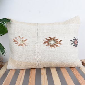 May include: A white throw pillow with a woven design featuring three geometric patterns in shades of brown, green, and orange.