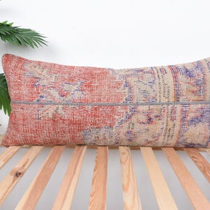 May include: A long rectangular pillow with a red, blue, and beige patterned design. The pillow is made from a woven fabric with a distressed look.