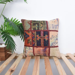 May include: A square throw pillow with a patchwork design featuring various shades of red, orange, blue, and beige. The pillow is made of woven fabric and has a frayed edge.