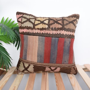 May include: A decorative pillow with a colorful geometric pattern in shades of brown, pink, red, and blue. The pillow is made from a woven fabric with a vintage look.