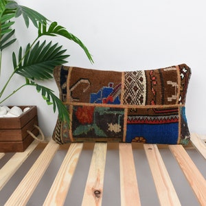 Puede incluir: Una almohada rectangular con un diseño de patchwork que presenta varios colores y patrones, incluyendo marrón, azul, rojo y verde. La almohada está hecha de tejido tejido y tiene una superficie ligeramente texturizada.