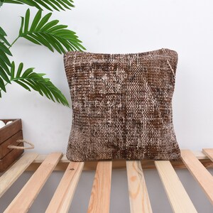 May include: A brown and white patterned throw pillow with a woven texture. The pillow is sitting on a wooden slatted surface.